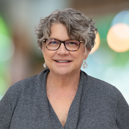 A woman wearing glasses and earrings is smiling for the camera.