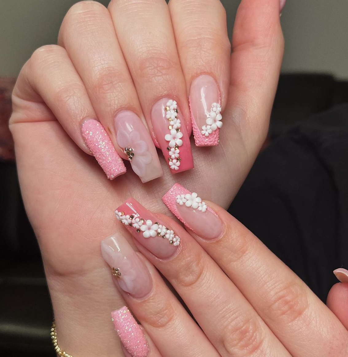 A close up of a woman 's hand with pink nails and white flowers