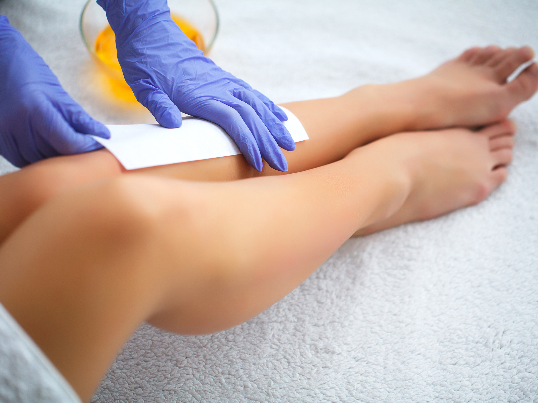 A woman is getting her legs waxed by a person wearing gloves.