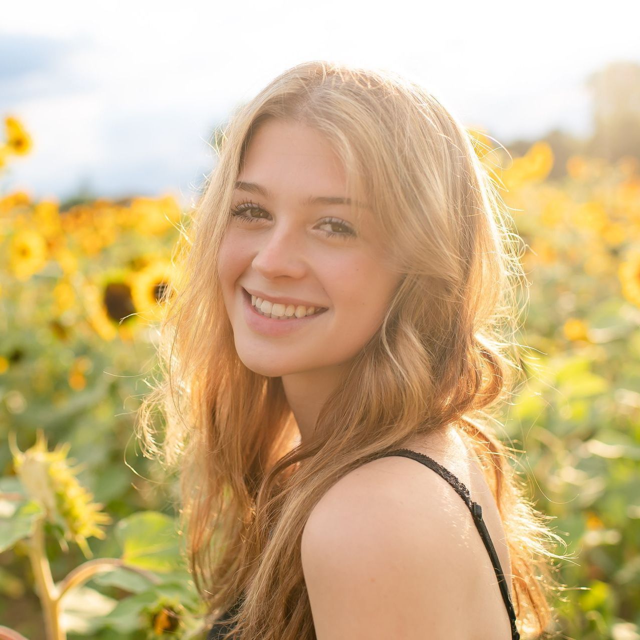 A woman is smiling in a field of sunflowers.