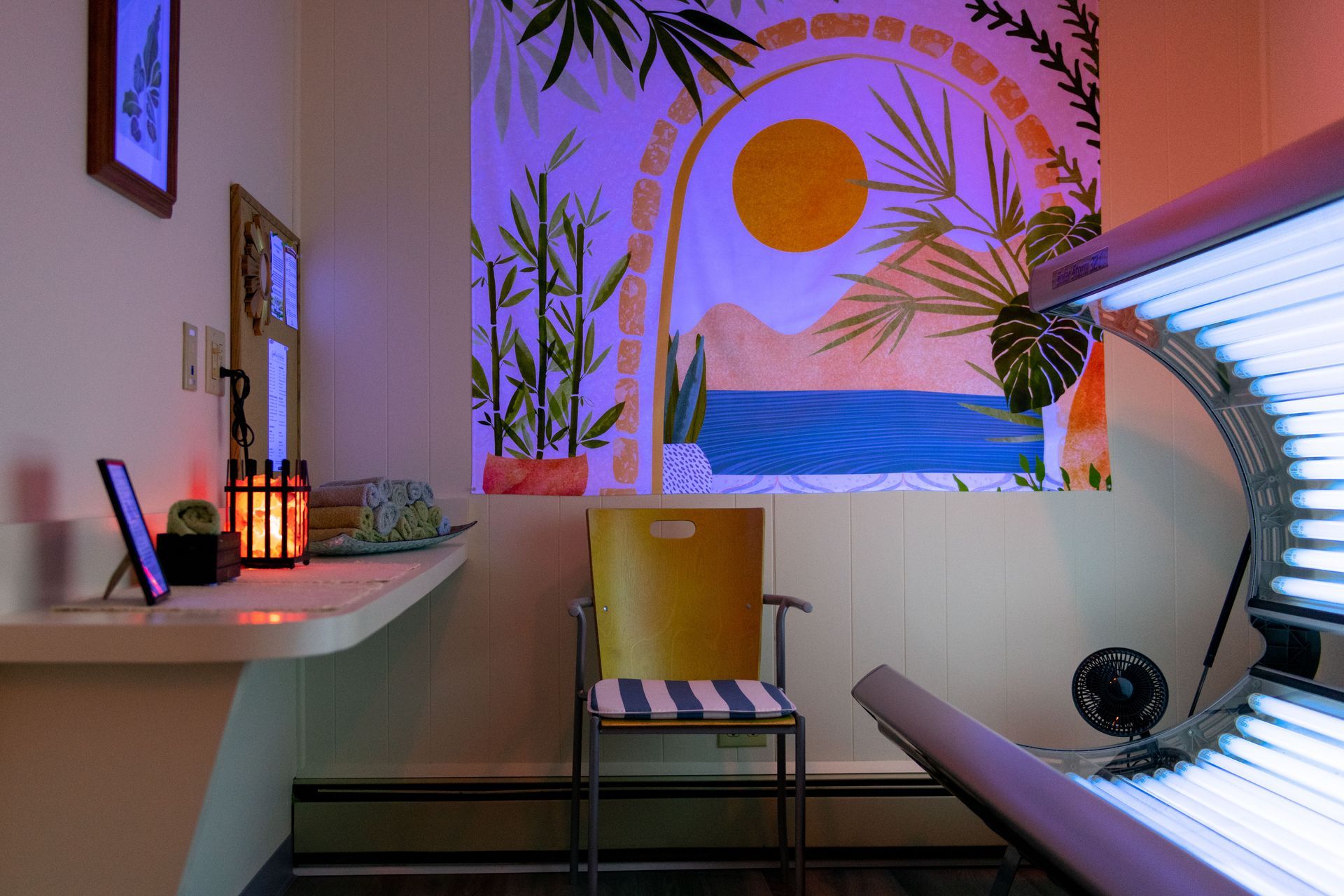 A room with a chair and a tanning bed with a painting on the wall