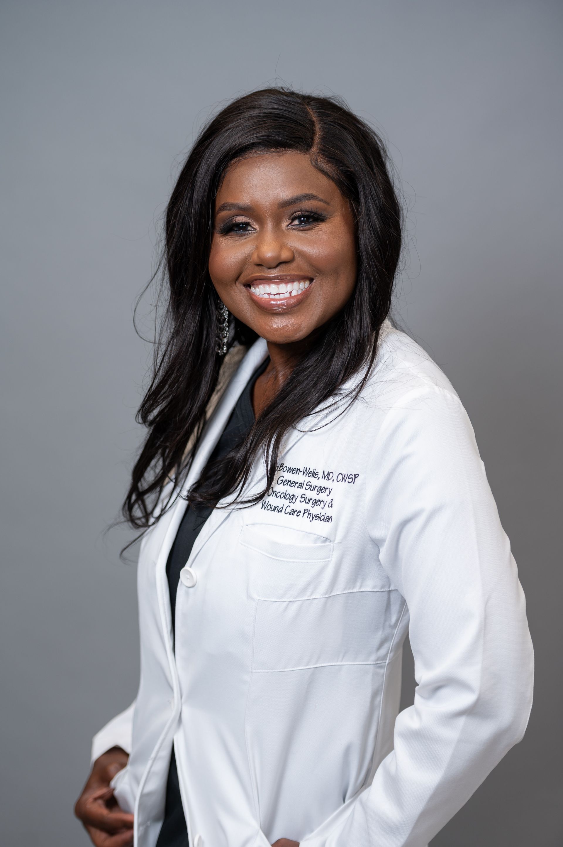 Woman in white lab coat smiles, stands against a gray backdrop. Woman in white lab coat smiles, stands against a gray backdrop.