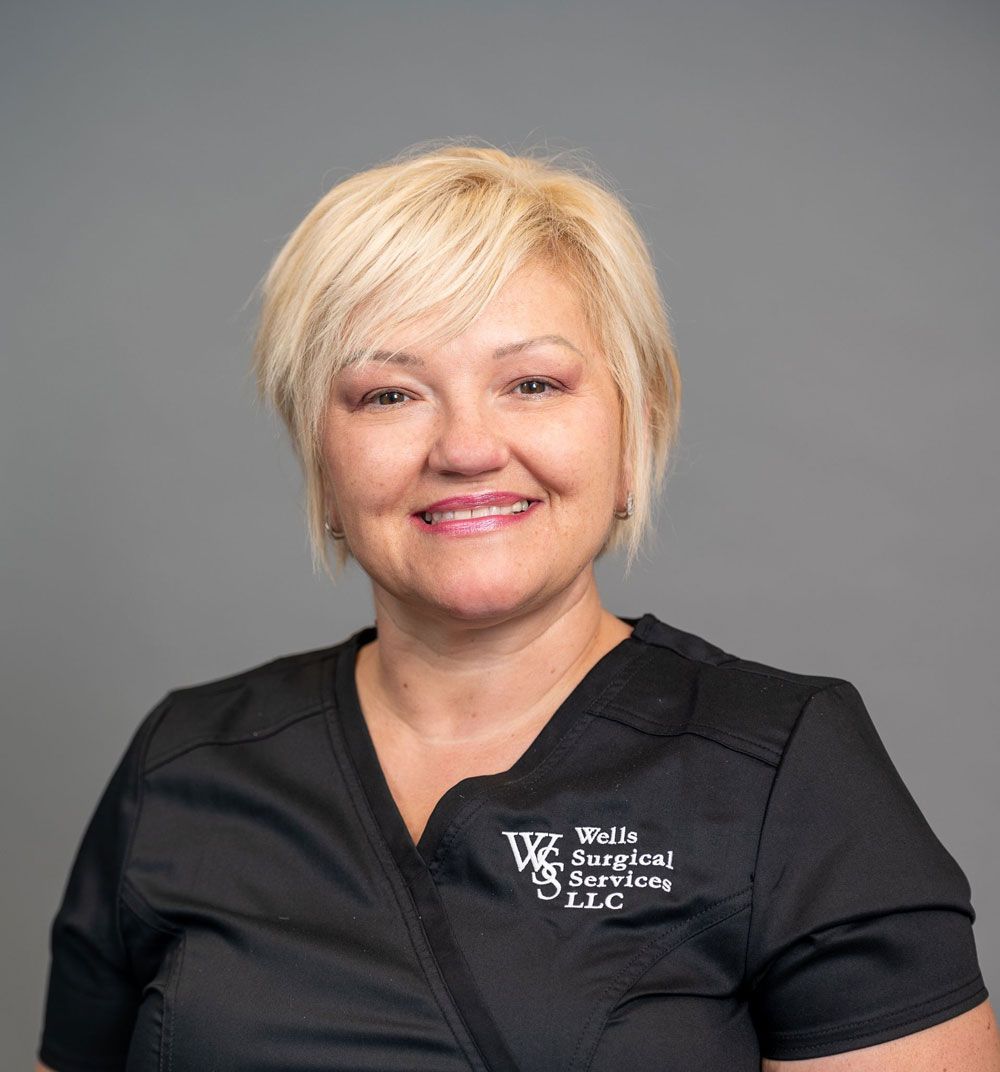 Woman with blonde hair wearing black scrubs smiles.