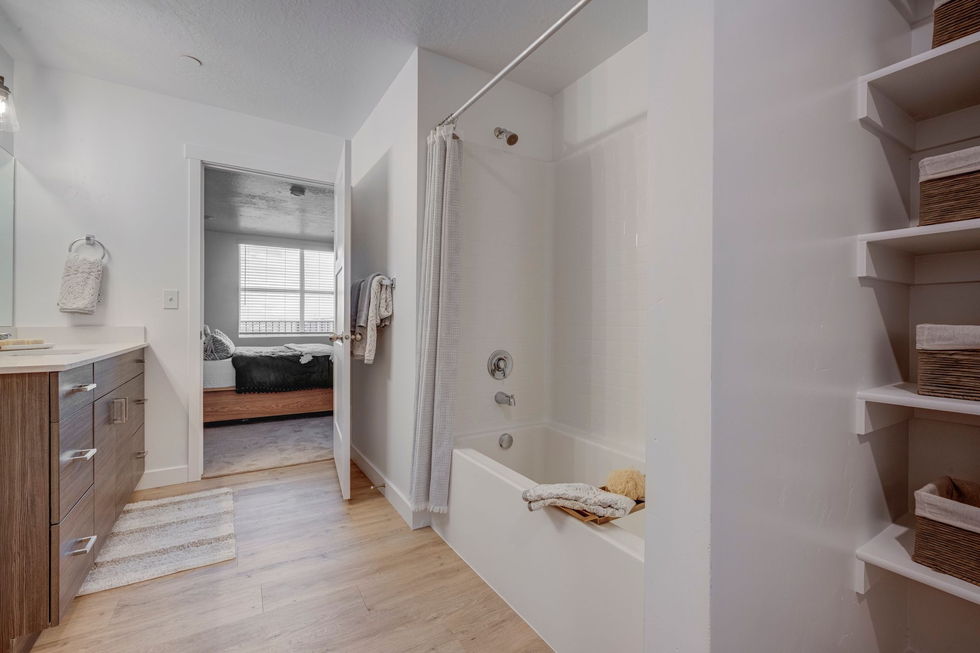 Bathroom with bathtub, open doorway to bedroom, vanity, and shelves at Sorella in Herriman, UT.