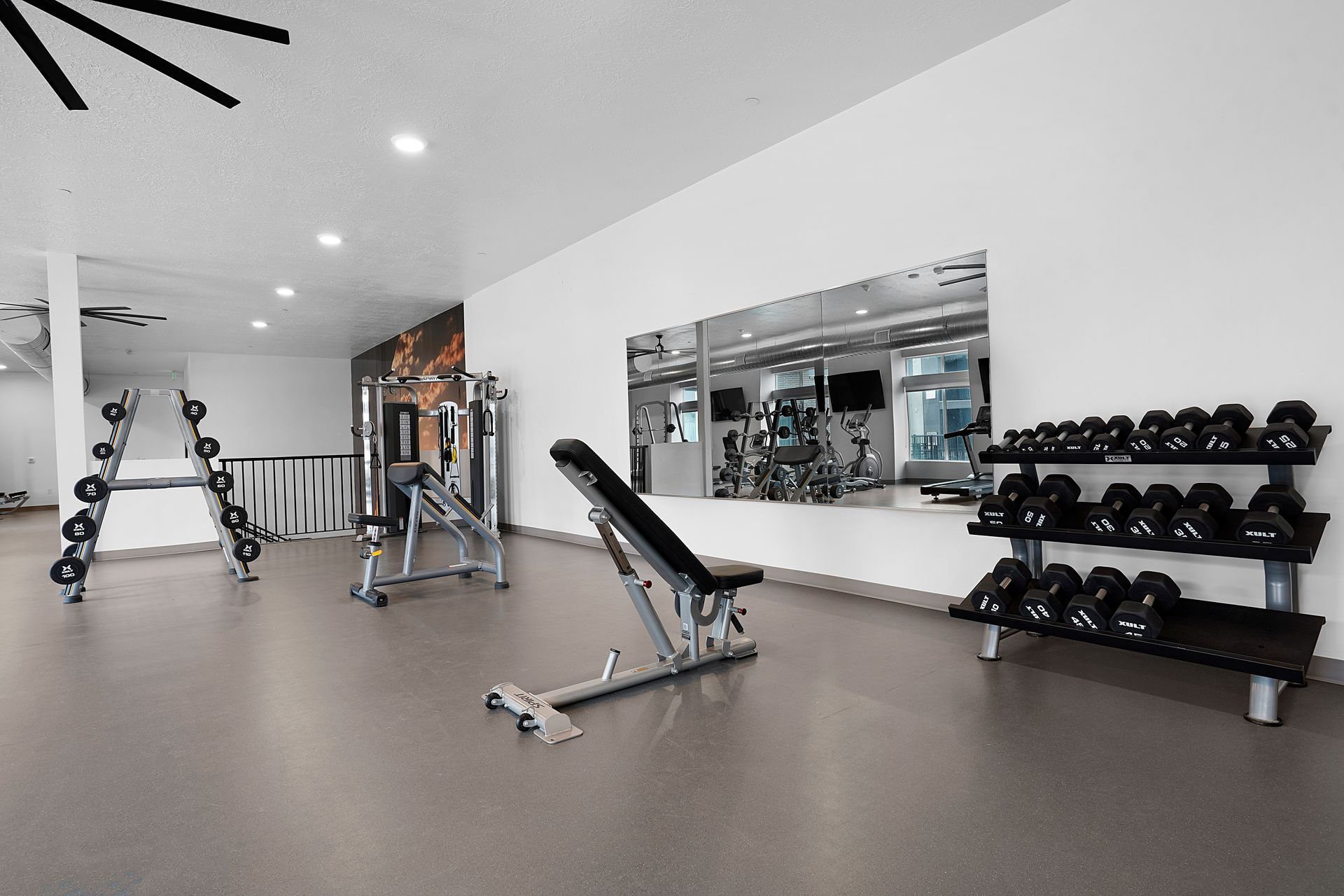 Gym with weight machines, dumbbells, a bench, and a large mirror at Sorella in Herriman, UT.
