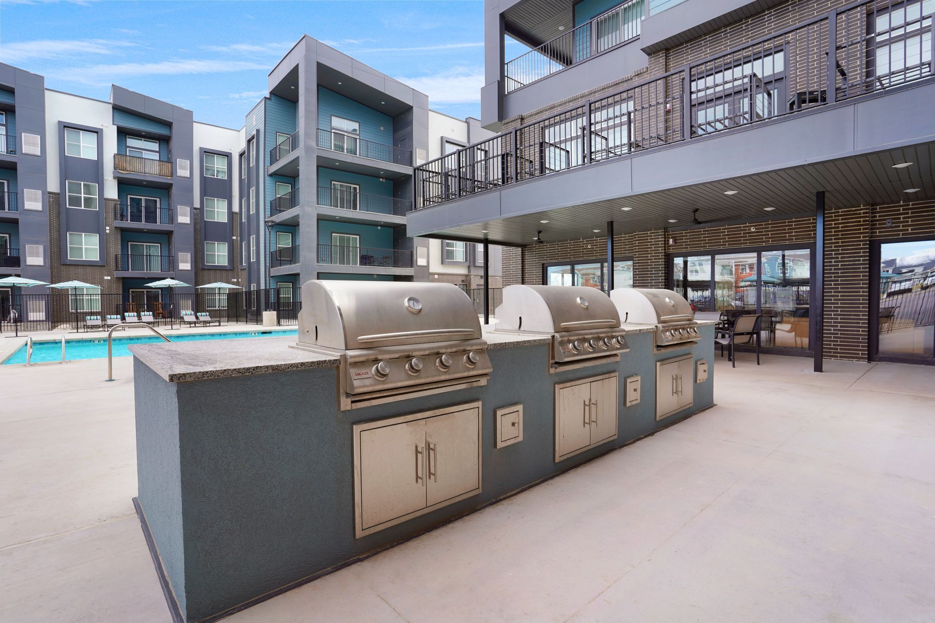 Outdoor grilling station with stainless steel grills, overlooking a pool and apartment building at Sorella in Herriman, UT.