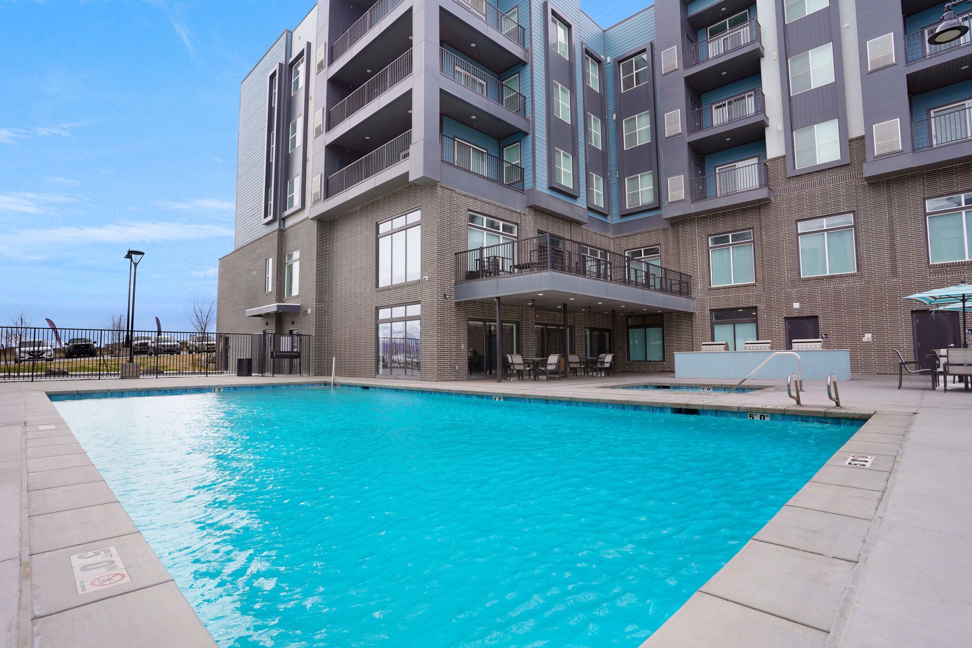 Swimming pool in front of a modern apartment building with a blue sky and patio furniture at Sorella in Herriman, UT.