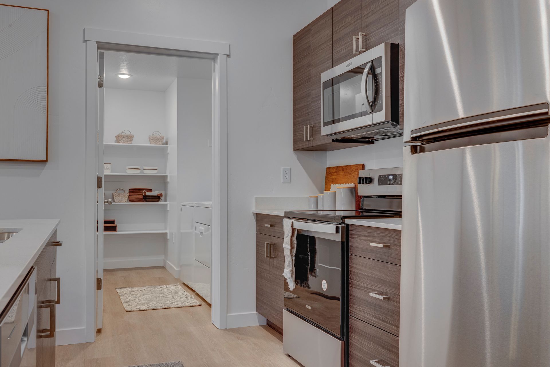 Kitchen with stainless steel appliances, dark cabinets, and a pantry with shelves at Sorella in Herriman, UT.