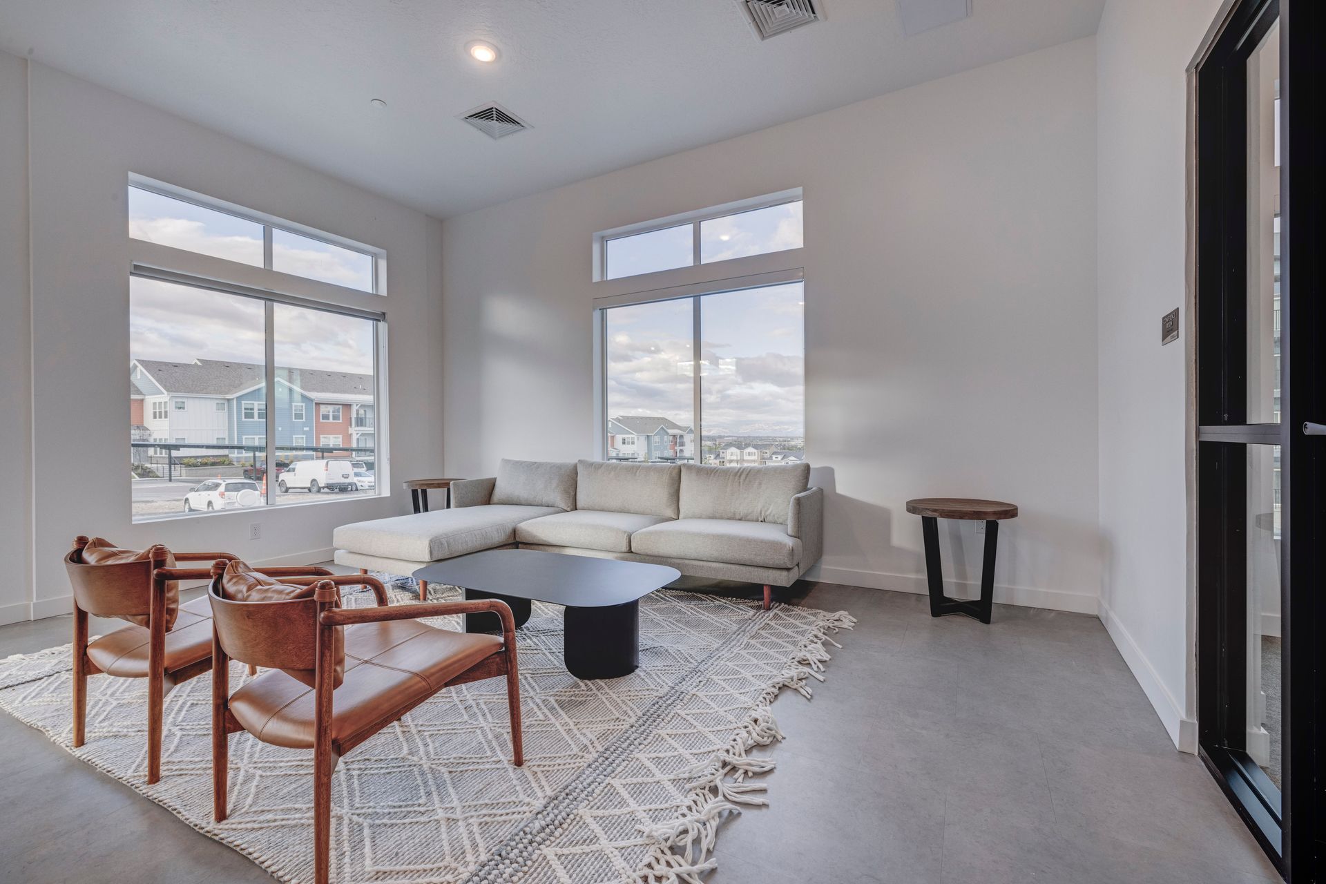 Modern living room with a sectional sofa, two chairs, and a rug. Large windows and concrete floor at Sorella in Herriman, UT.