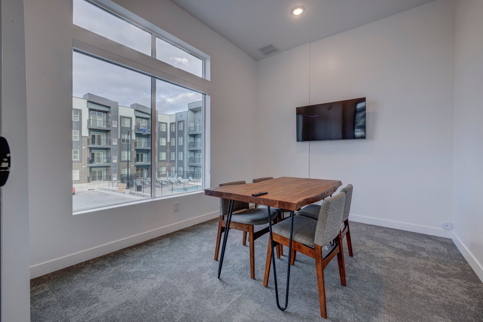 Meeting room with a wooden table, chairs, TV, and large window overlooking an apartment complex at Sorella in Herriman, UT.