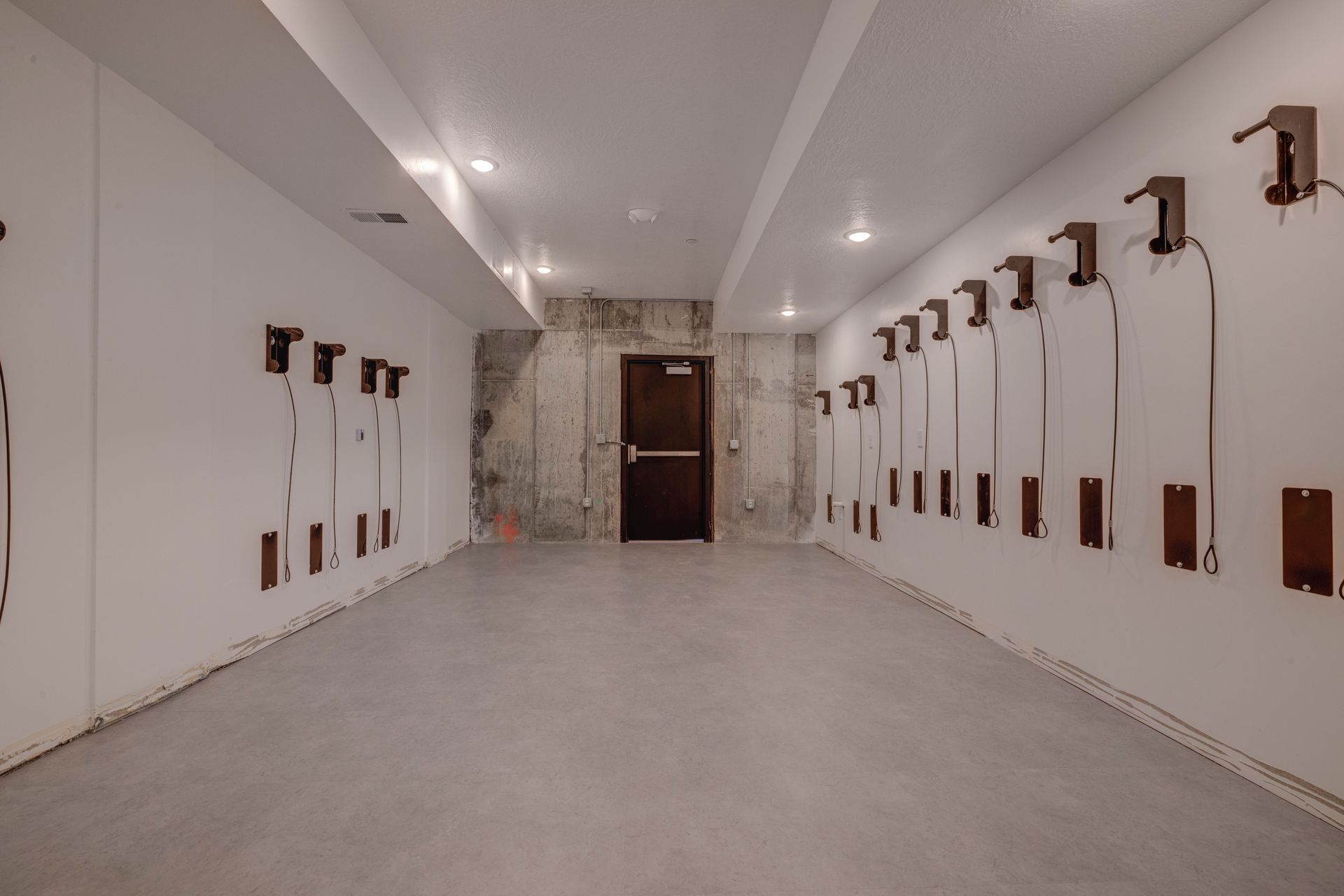 Long hallway with white walls and exposed wiring, a closed brown door at the end at Sorella in Herriman, UT.