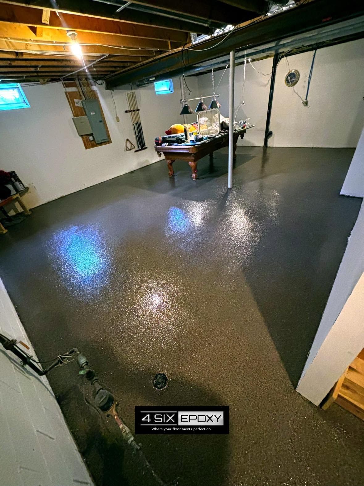 Basement room with wet gray floor, exposed ceiling beams, and a table against the far wall.