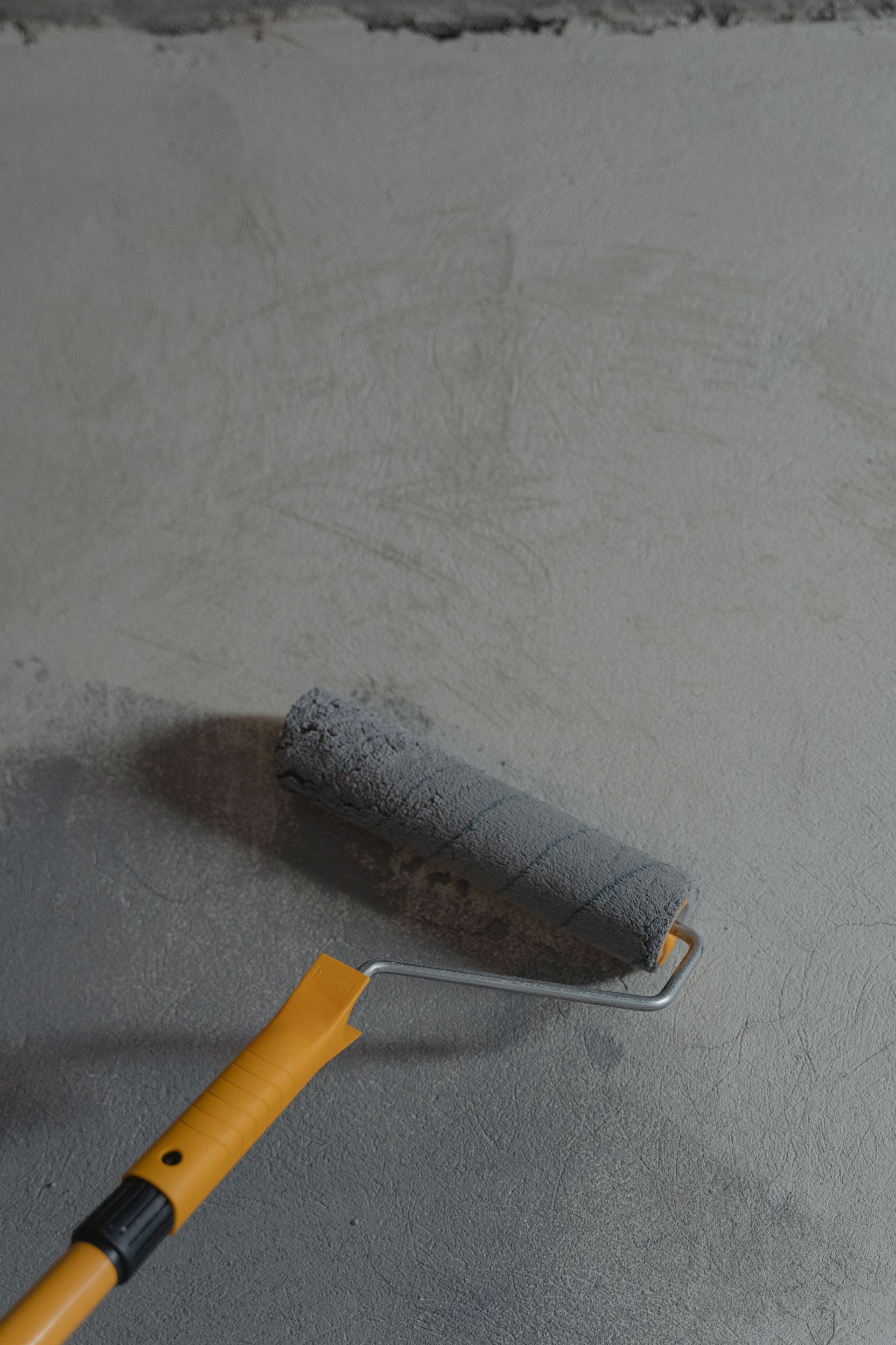 Paint roller applying gray paint to a wall corner, with an orange handle in view
