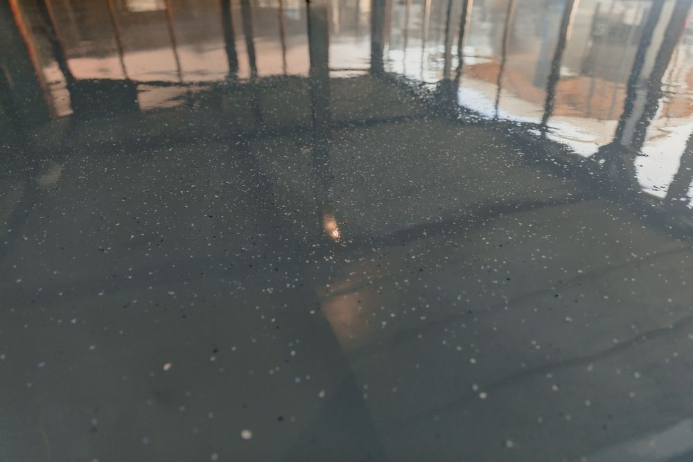 Rain-speckled dark pavement reflecting windows and lights indoors