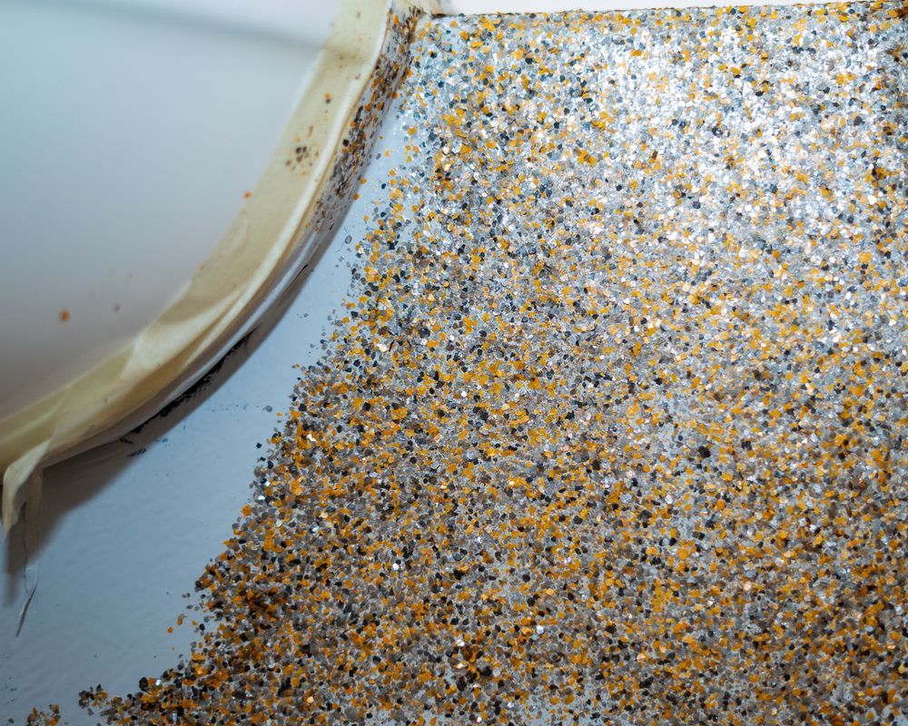 Close-up of gold glitter or confetti spilled on a white surface beside a plastic container lid.