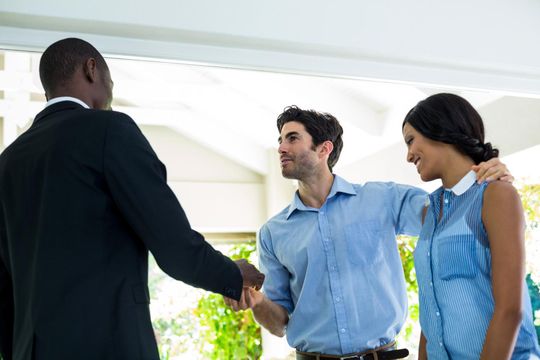 Three people shake hands in a bright office setting.