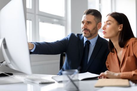 Two professionals reviewing data on a desktop computer in a bright office