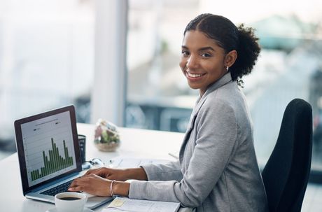 Woman smiling at a desk using a laptop with analytics charts on screen