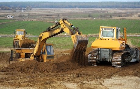 Two yellow bulldozers moving dirt on a construction site in a rural field