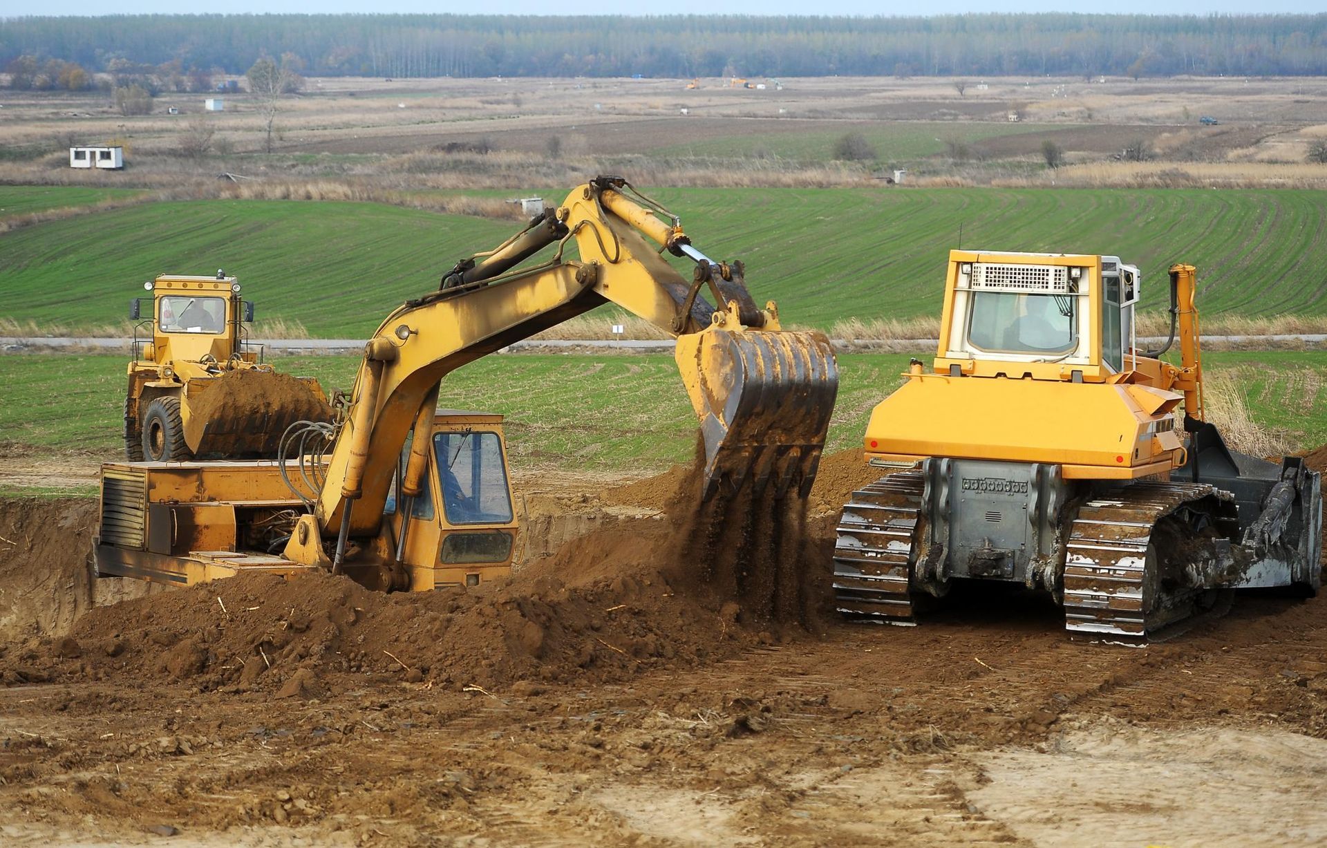 Yellow excavators and a bulldozer working on a dirt field, moving soil.