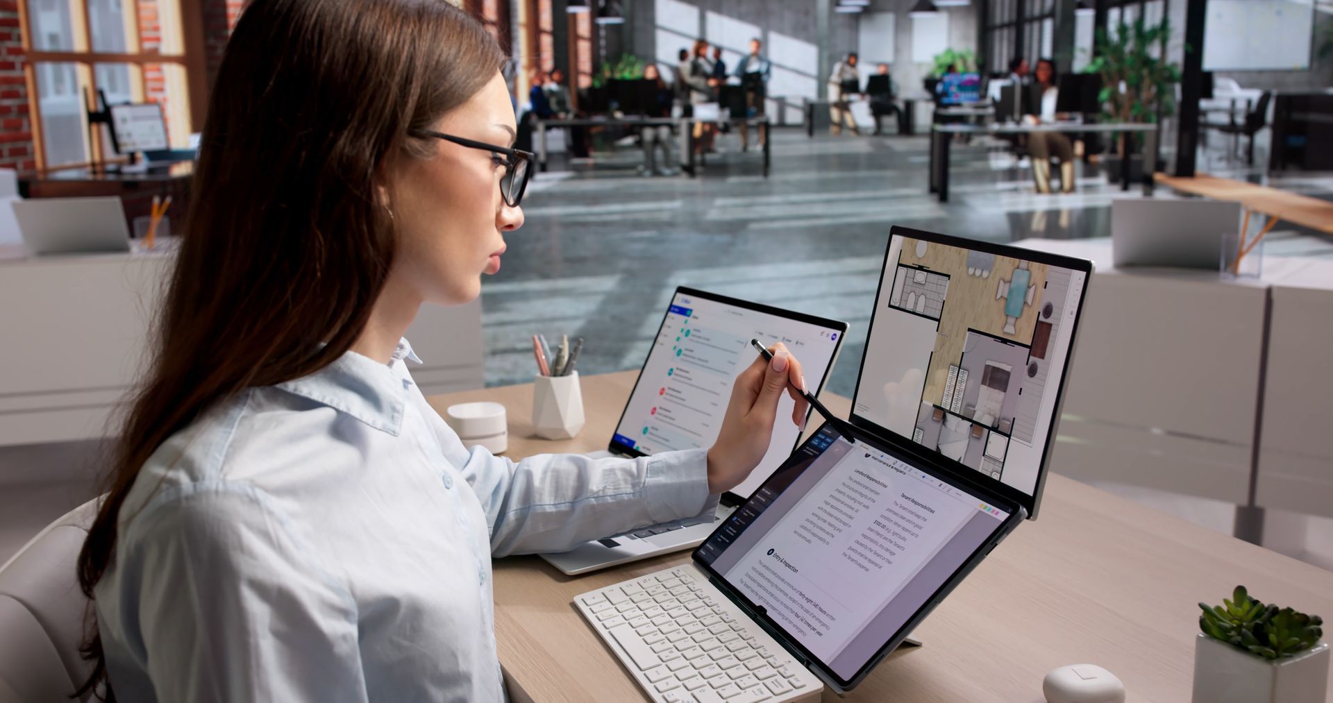 Woman reviewing documents on a laptop and tablet at a desk in a bright open office.