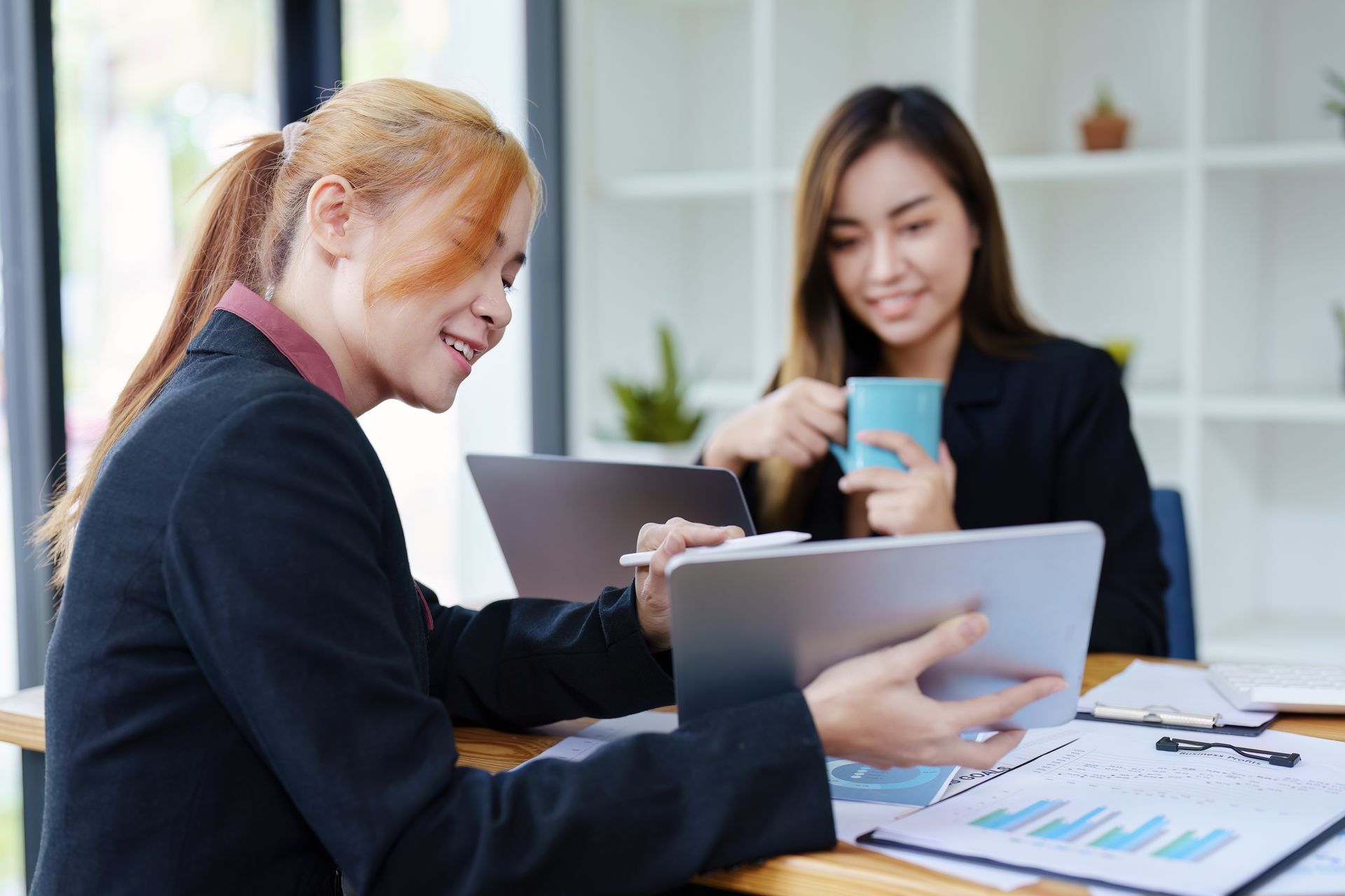 Two coworkers smiling and discussing a tablet in a bright office meeting space