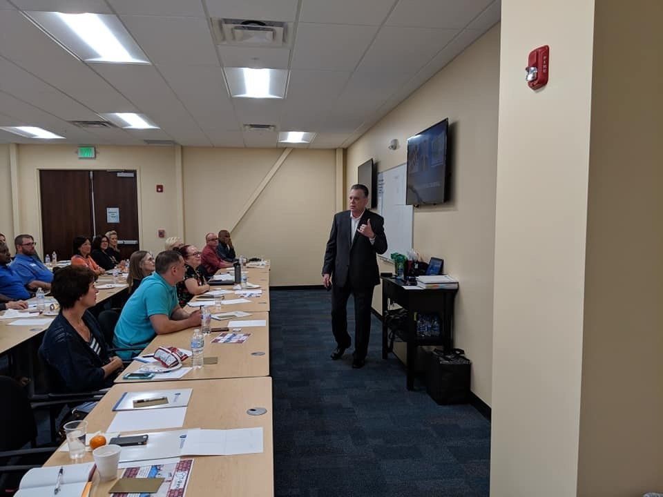 A man is giving a presentation to a group of people sitting at tables.