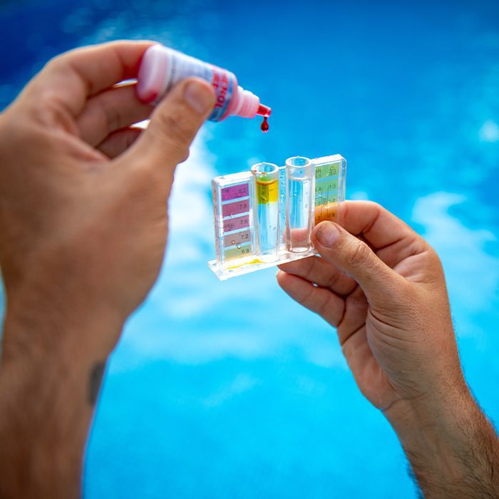 Hands holding a test strip and dropping liquid into a small color-coded water test kit against a blue background