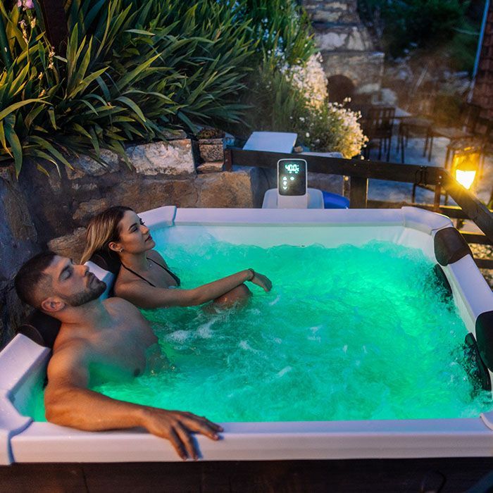 Two people relaxing in a glowing hot tub at dusk, surrounded by plants and stone steps.