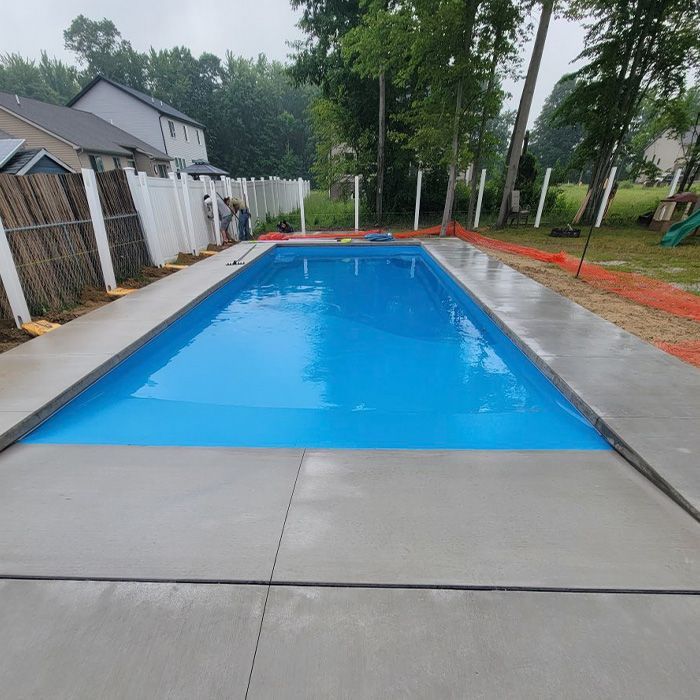 Backyard swimming pool with blue cover, concrete deck, and trees along the fence