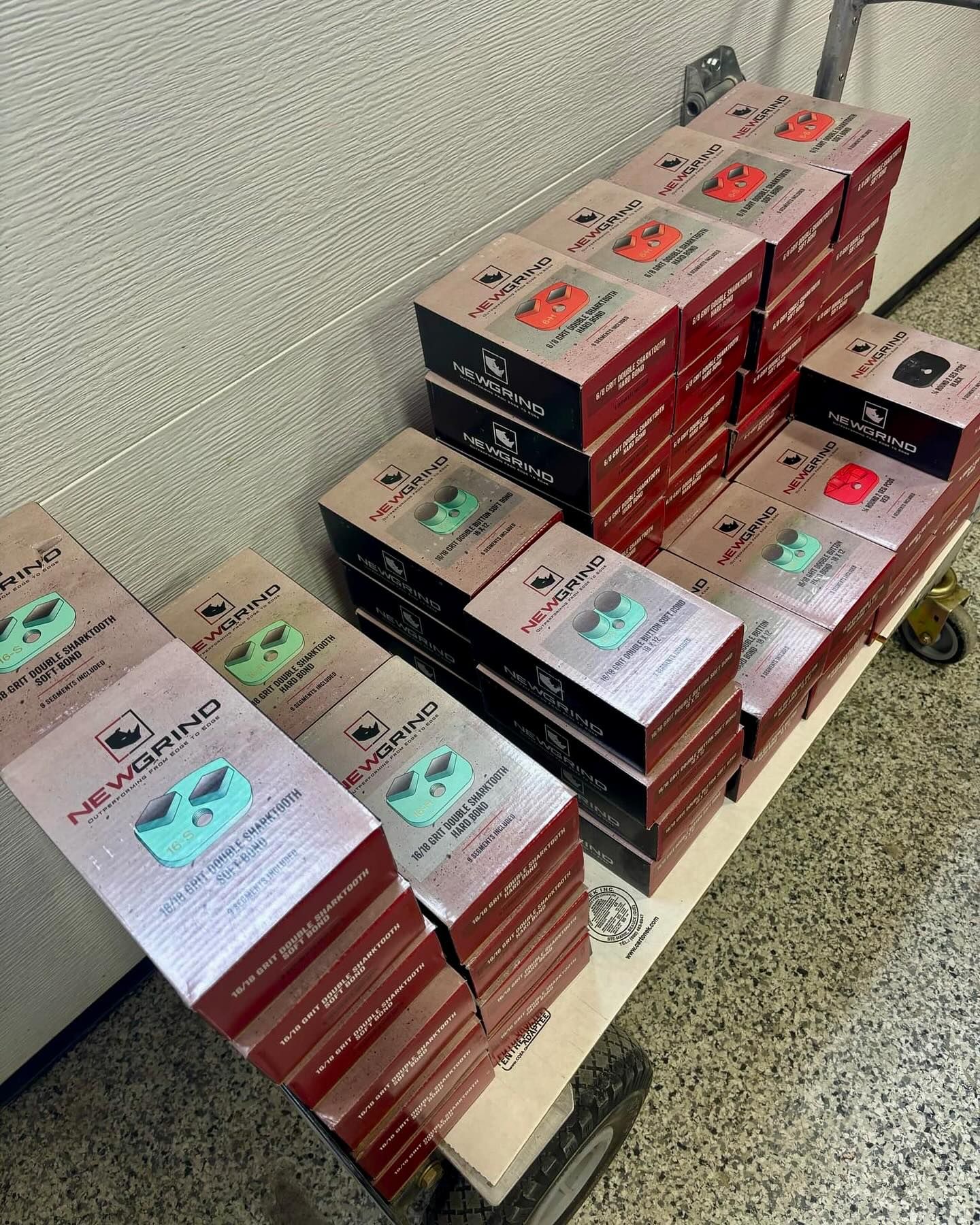 Des piles de produits en boîtes rouges et argentées sont disposées sur une palette en bois dans une allée d'entrepôt.