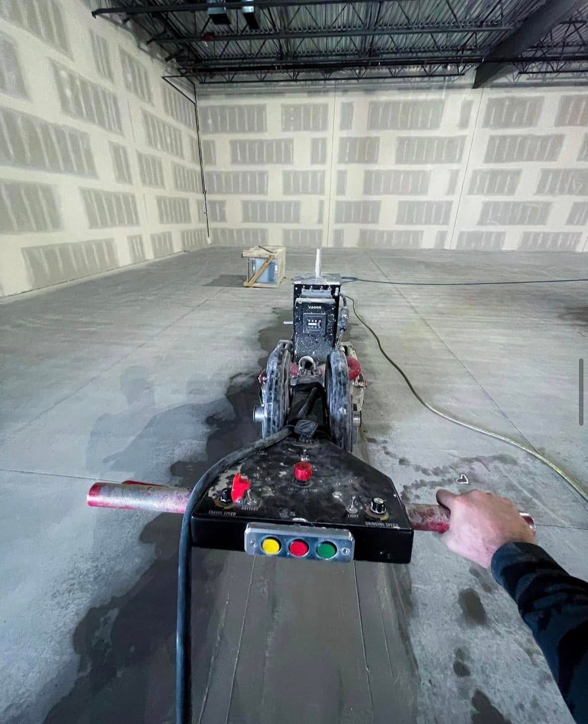 Une personne pousse une machine à polir dans une pièce en béton brut aux murs de parpaings.