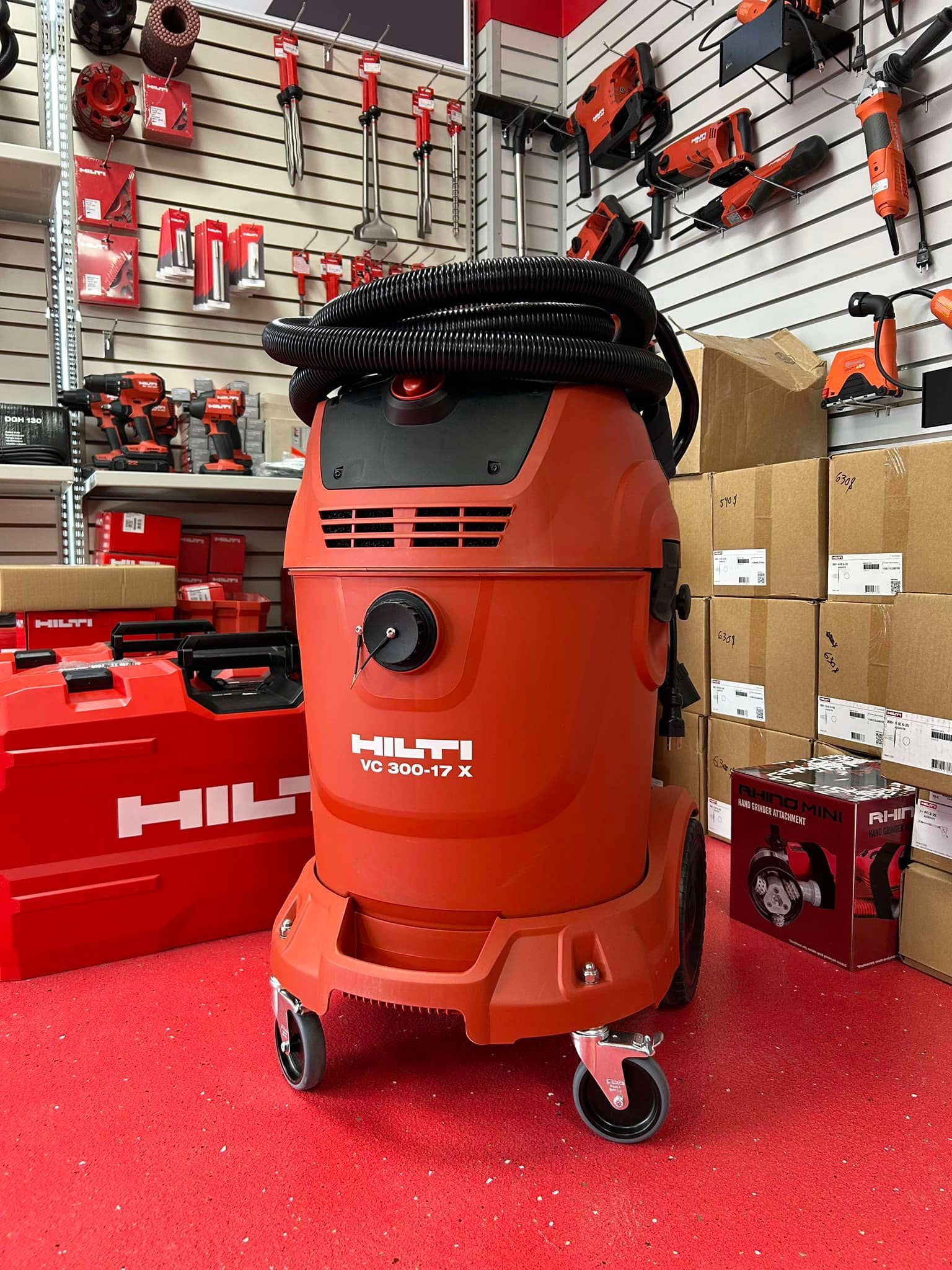 Aspirateur eau et poussière Hilti orange et noir sur moquette rouge dans une vitrine de magasin d'outillage