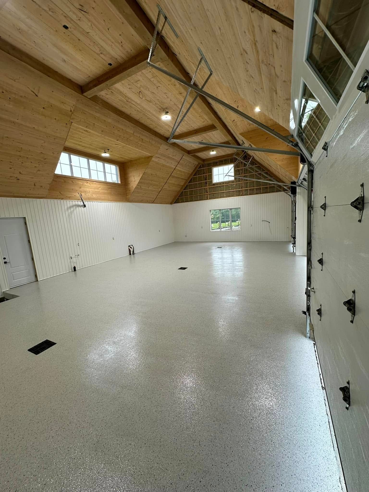 Pièce spacieuse et vide avec plafond voûté en bois, murs blancs et sol en époxy moucheté