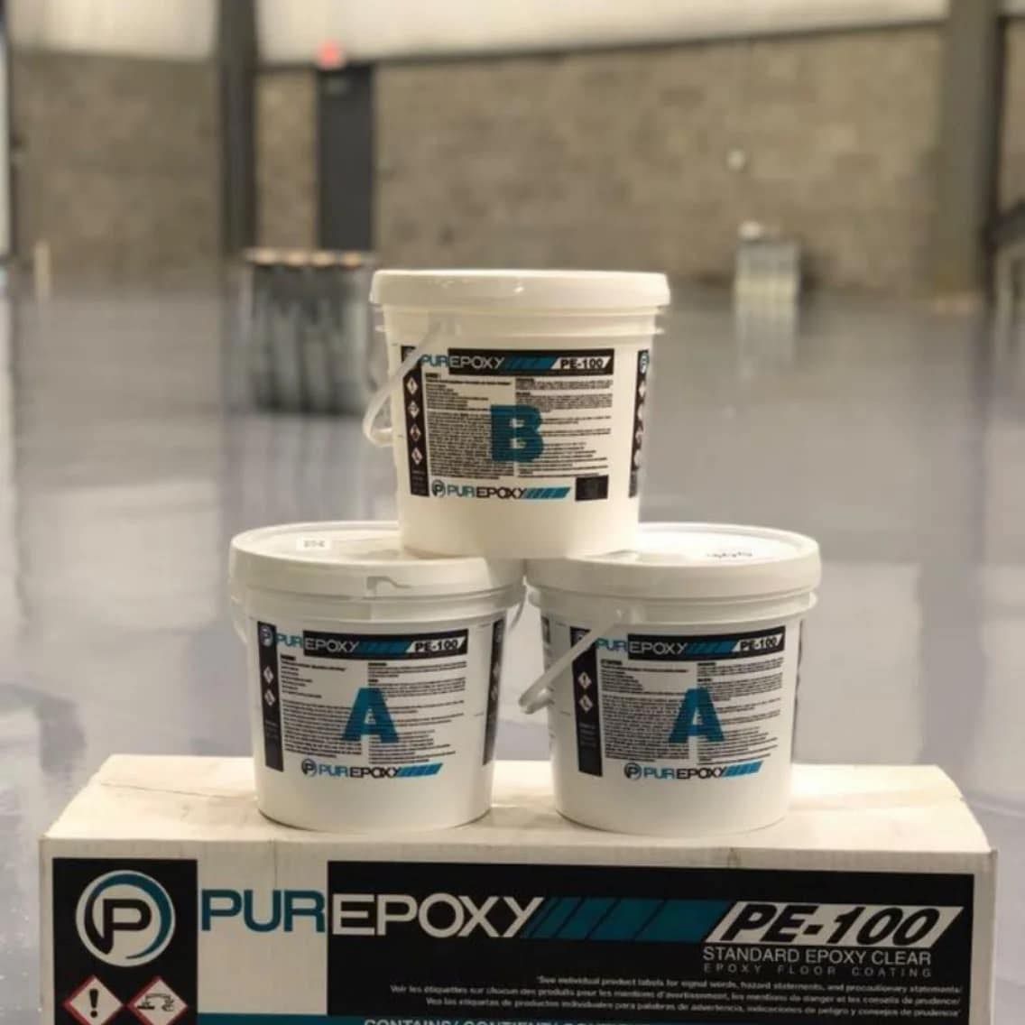 Trois pots blancs de produit PurePoxy empilés sur une boîte dans un entrepôt.