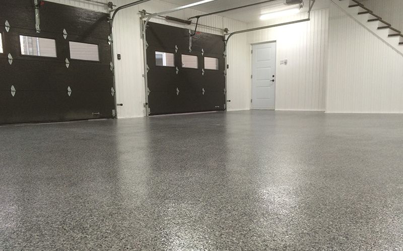 Garage intérieur vide avec portes noires, murs blancs et sol gris moucheté