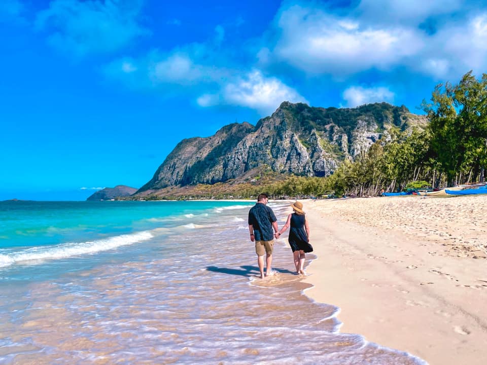 A man and a woman are walking on a beach holding hands.