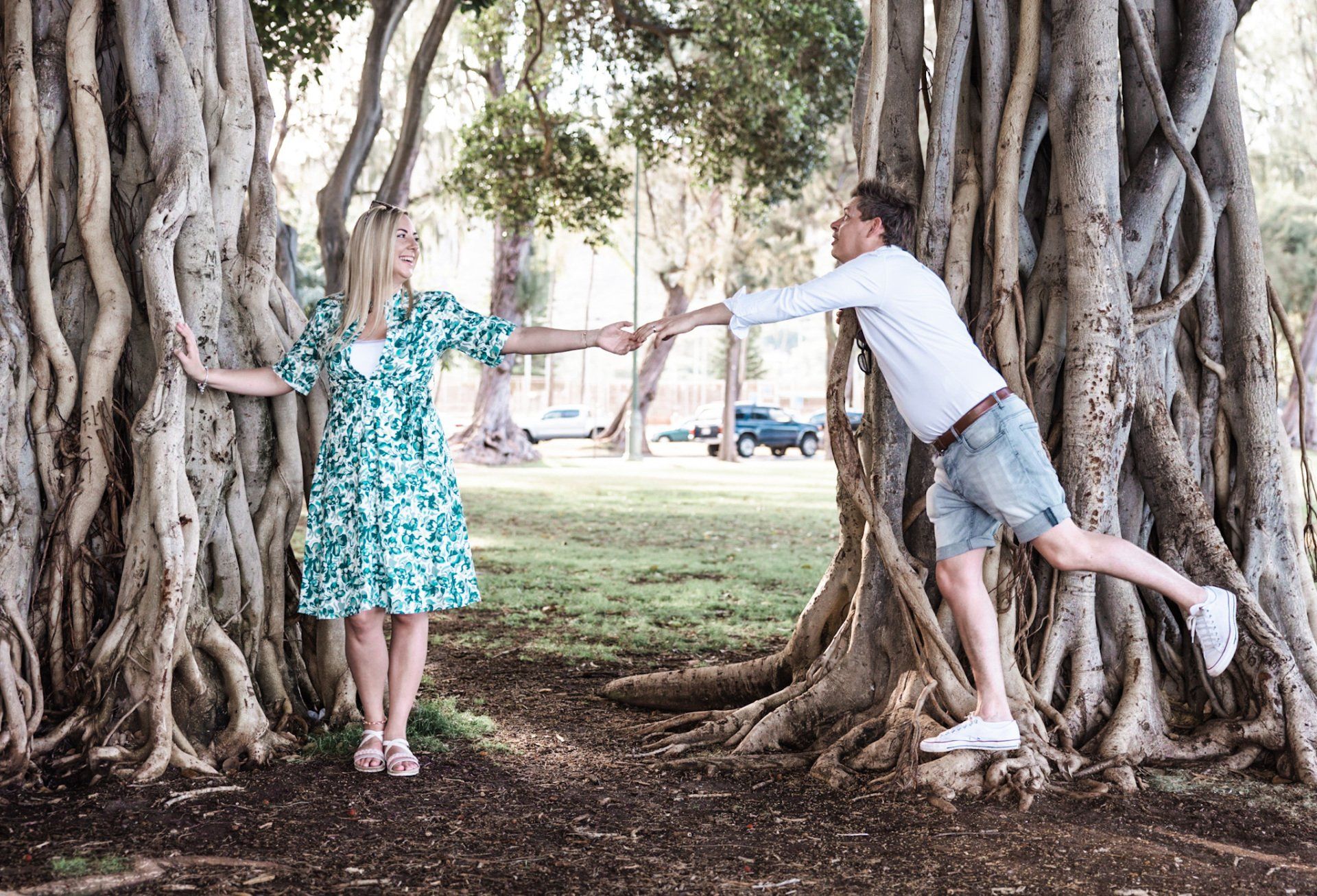 A man and a woman are hugging trees in a park.