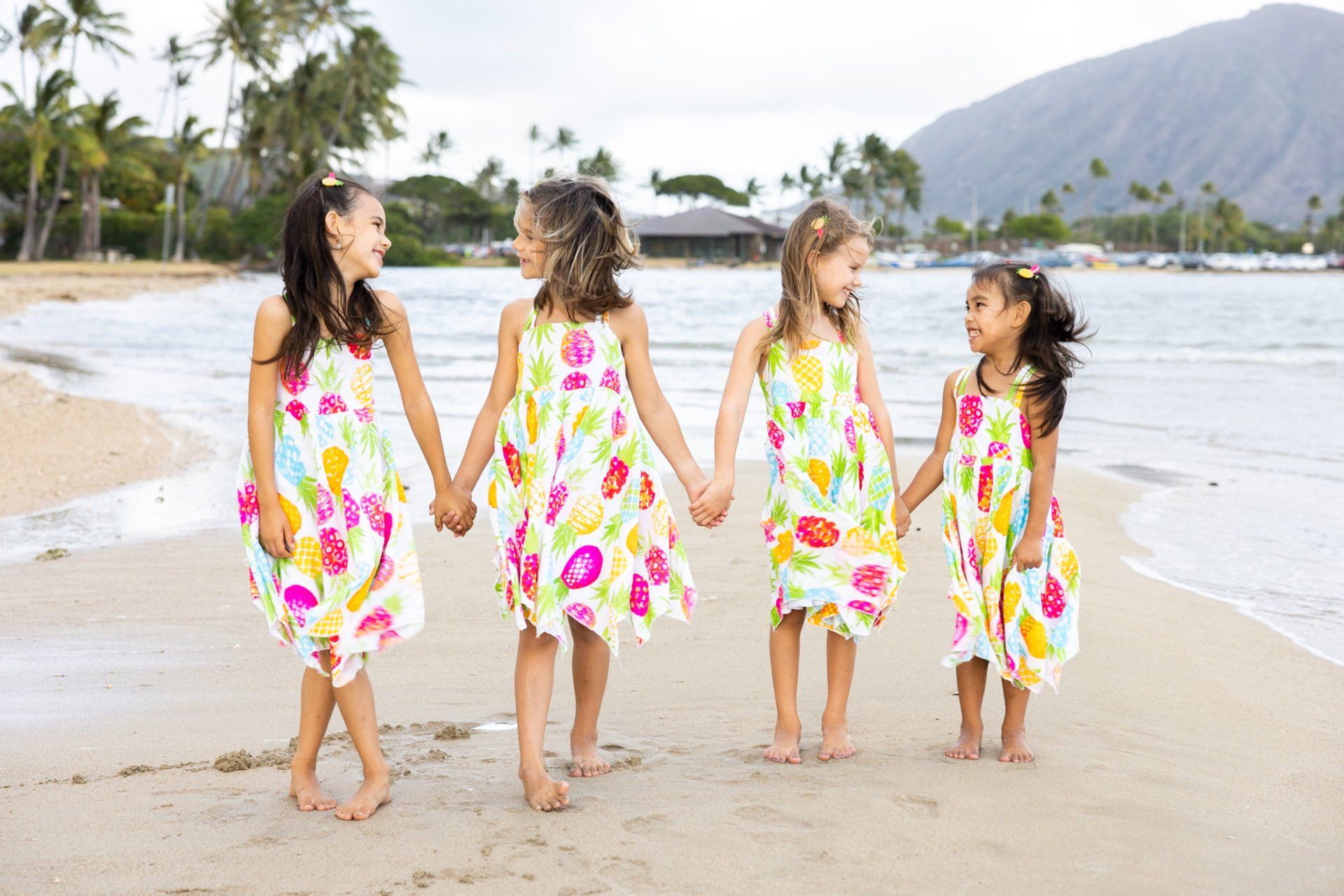 Four little girls are holding hands on the beach.
