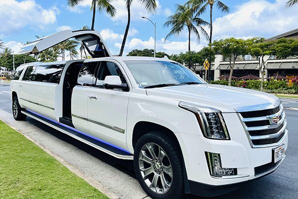 A white cadillac escalade limousine is parked on the side of the road.