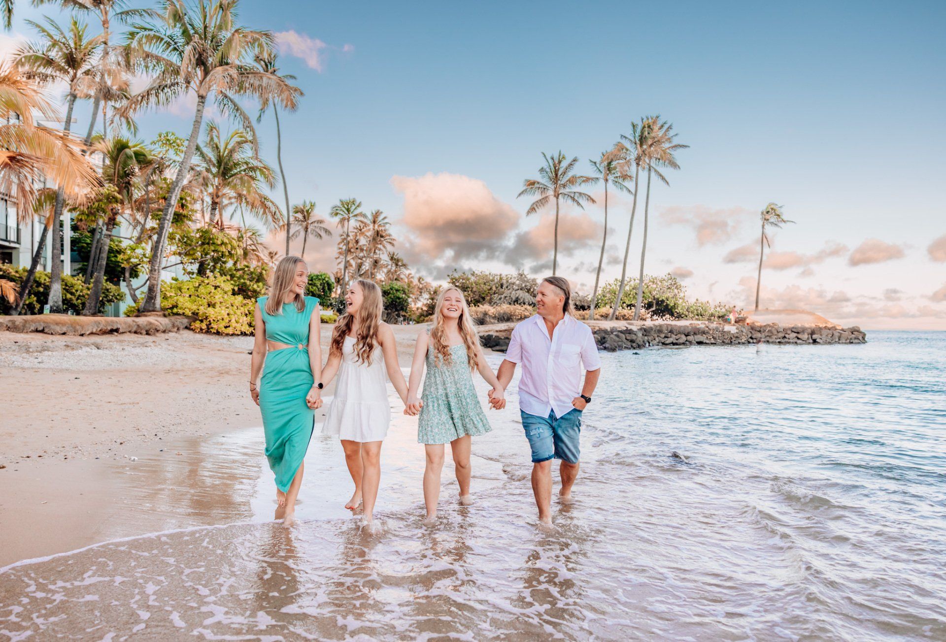 A family is walking along the beach holding hands.