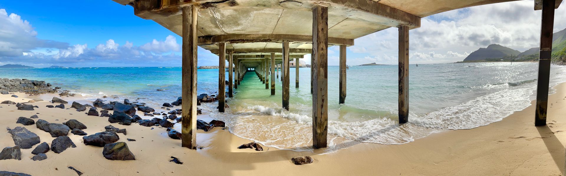 A pier leading into the ocean with a beach in the foreground.