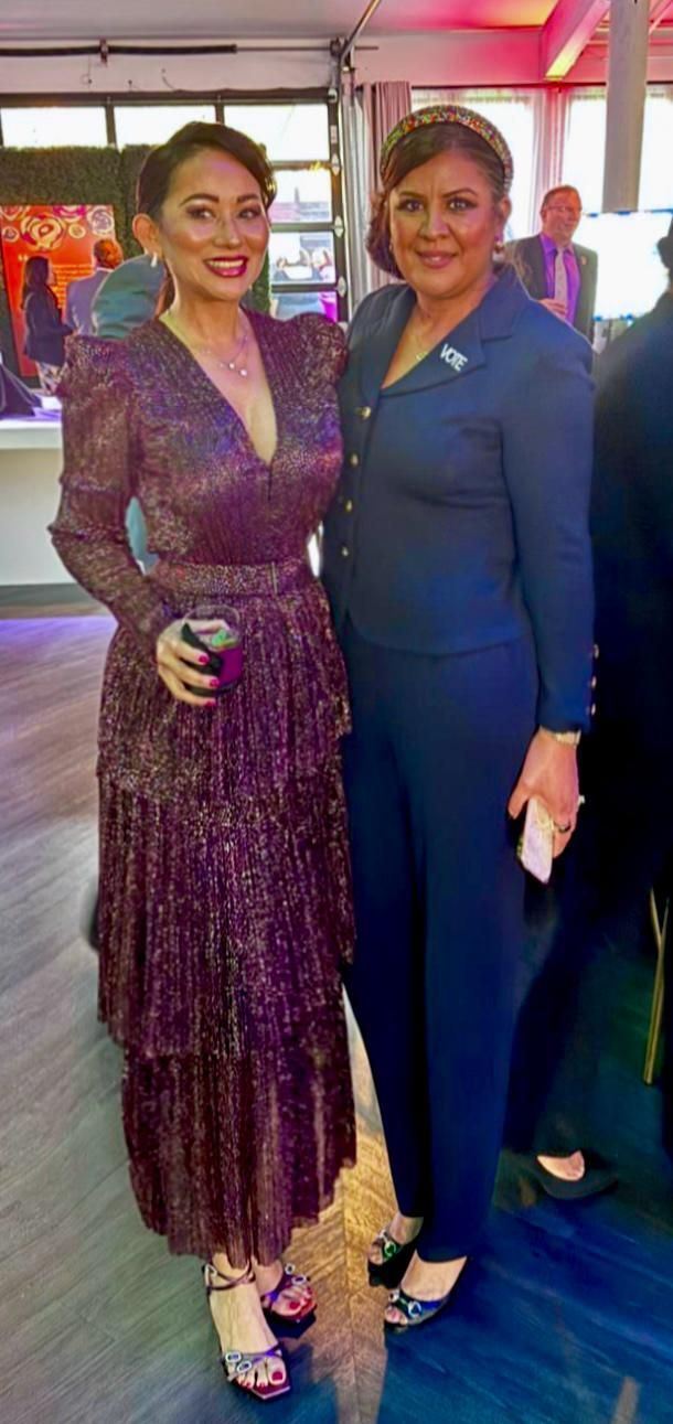 Two women are standing next to each other in a room . one of the women is wearing a purple dress.