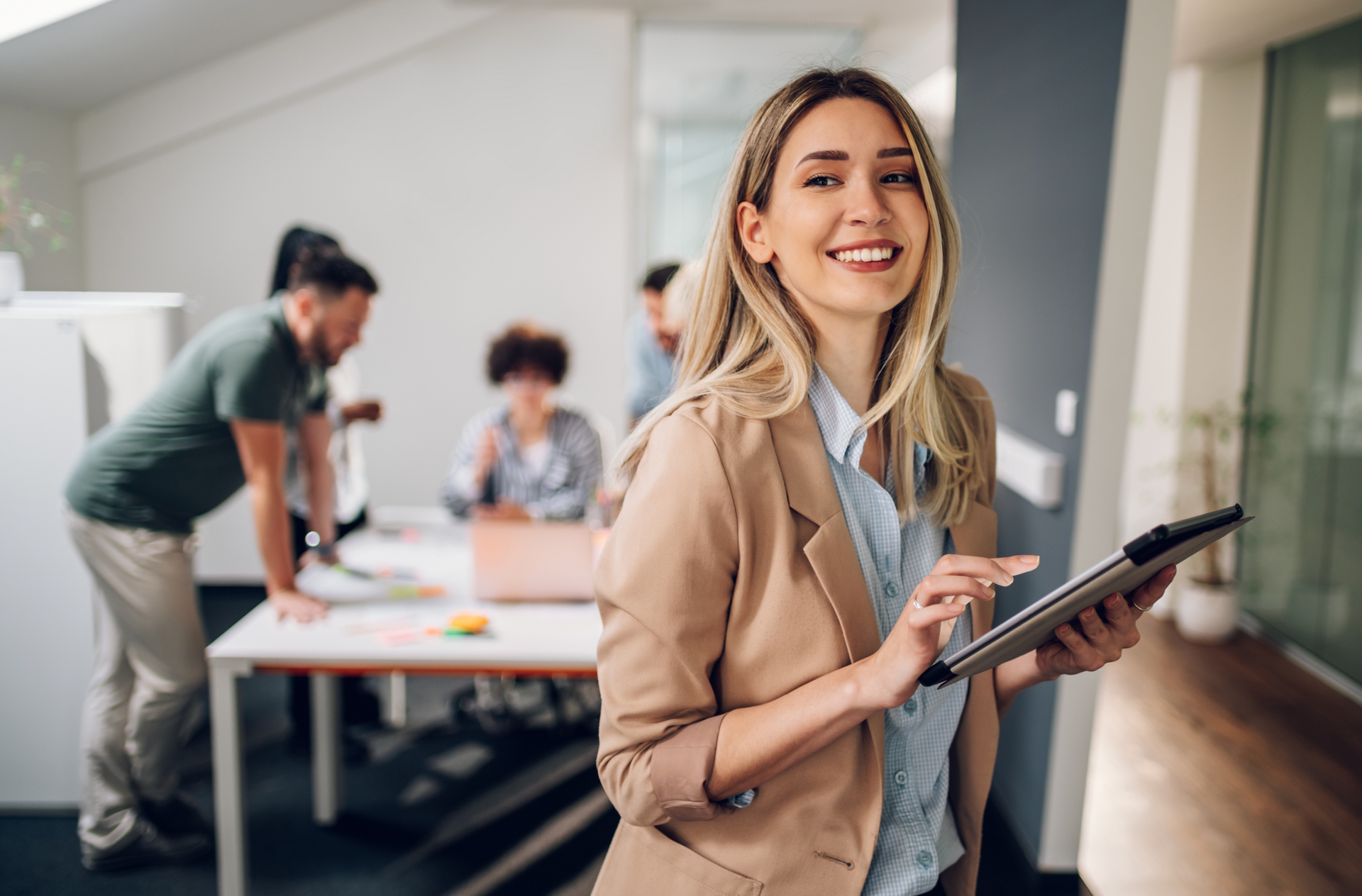 A woman is smiling while holding a tablet in an office.
