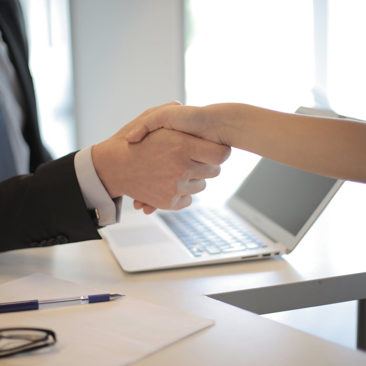 A man and woman shaking hands in front of a laptop