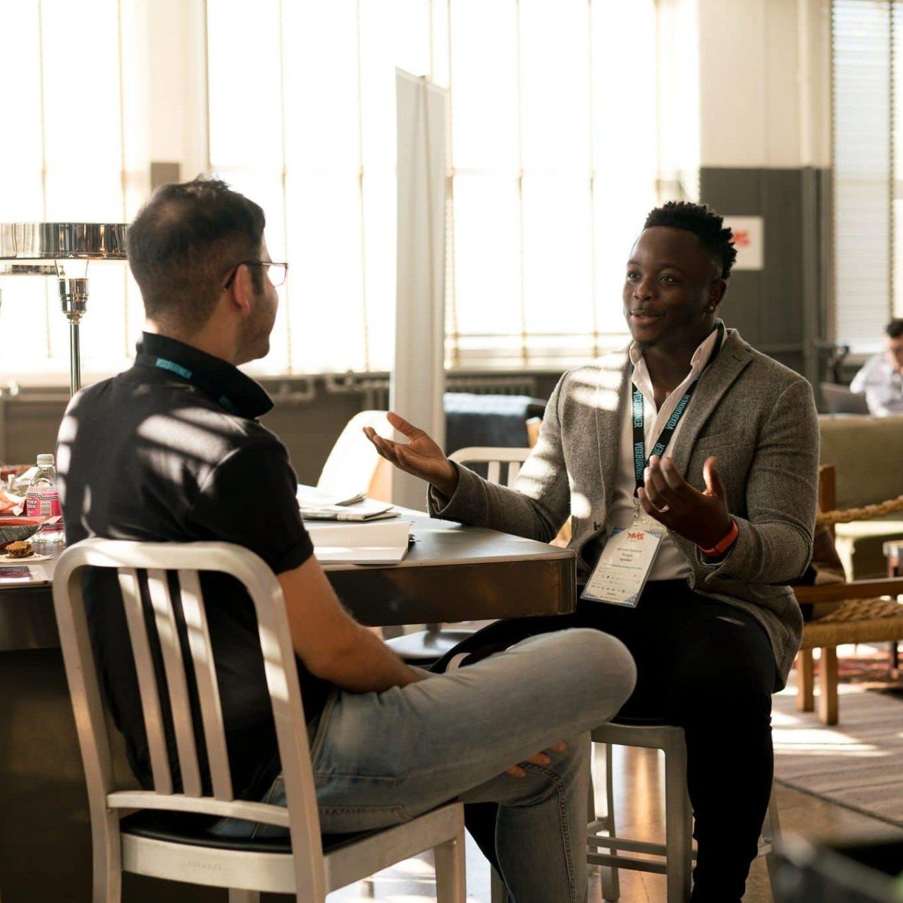 Two men are sitting at a table talking to each other.