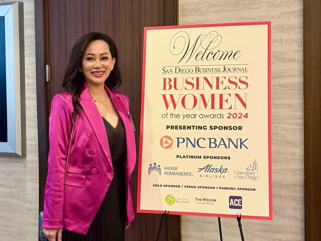 A woman in a pink jacket is standing in front of a sign that says welcome business women.