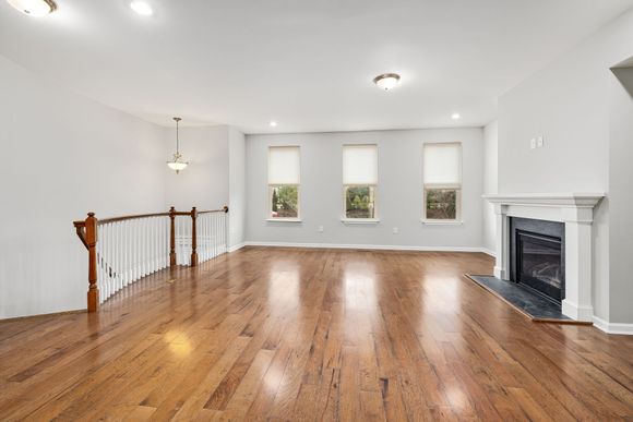 Empty living room with hardwood floors, three windows, and a white fireplace.