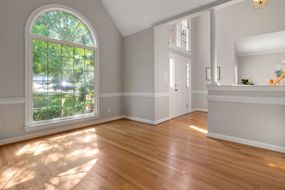 Bright empty living room with arched window, hardwood floors, and light gray walls