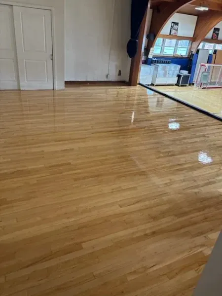 Empty living room with glossy red floors, staircase railing, and a kitchen area in the background